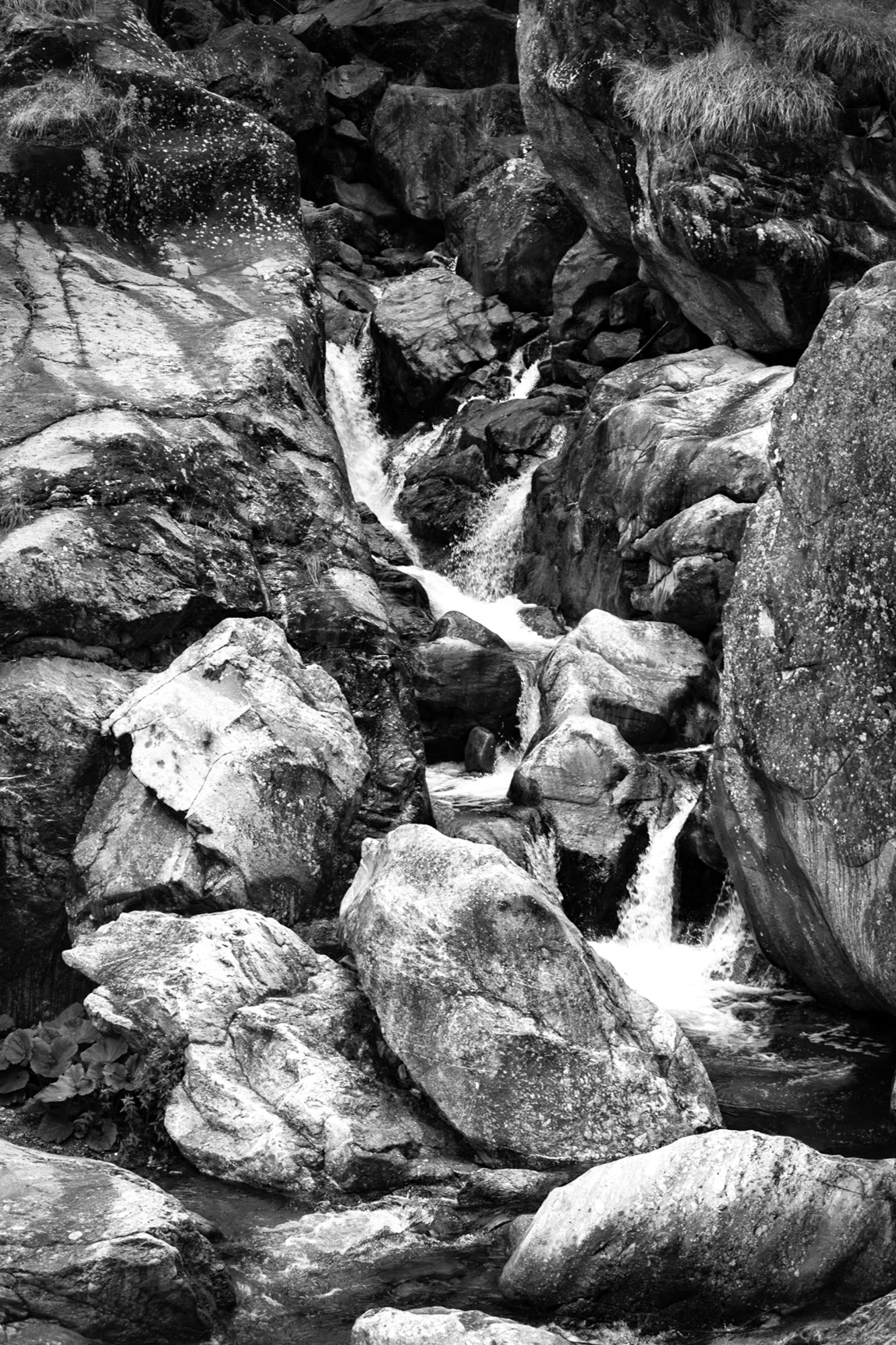 Cascade du Ray entre de gros blocs rocheux, eau qui s’écoule en marches successives, noir et blanc