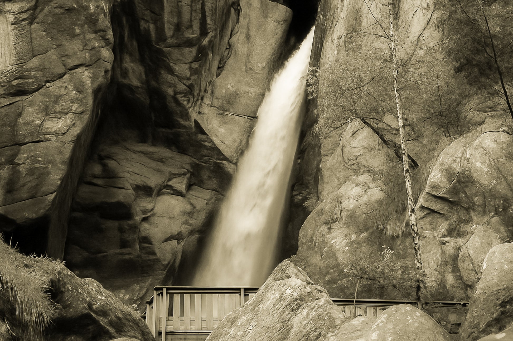 Grande chute d’eau de la cascade du Ray au fond d’une faille rocheuse, passerelle de bois au premier plan, rendu vintage
