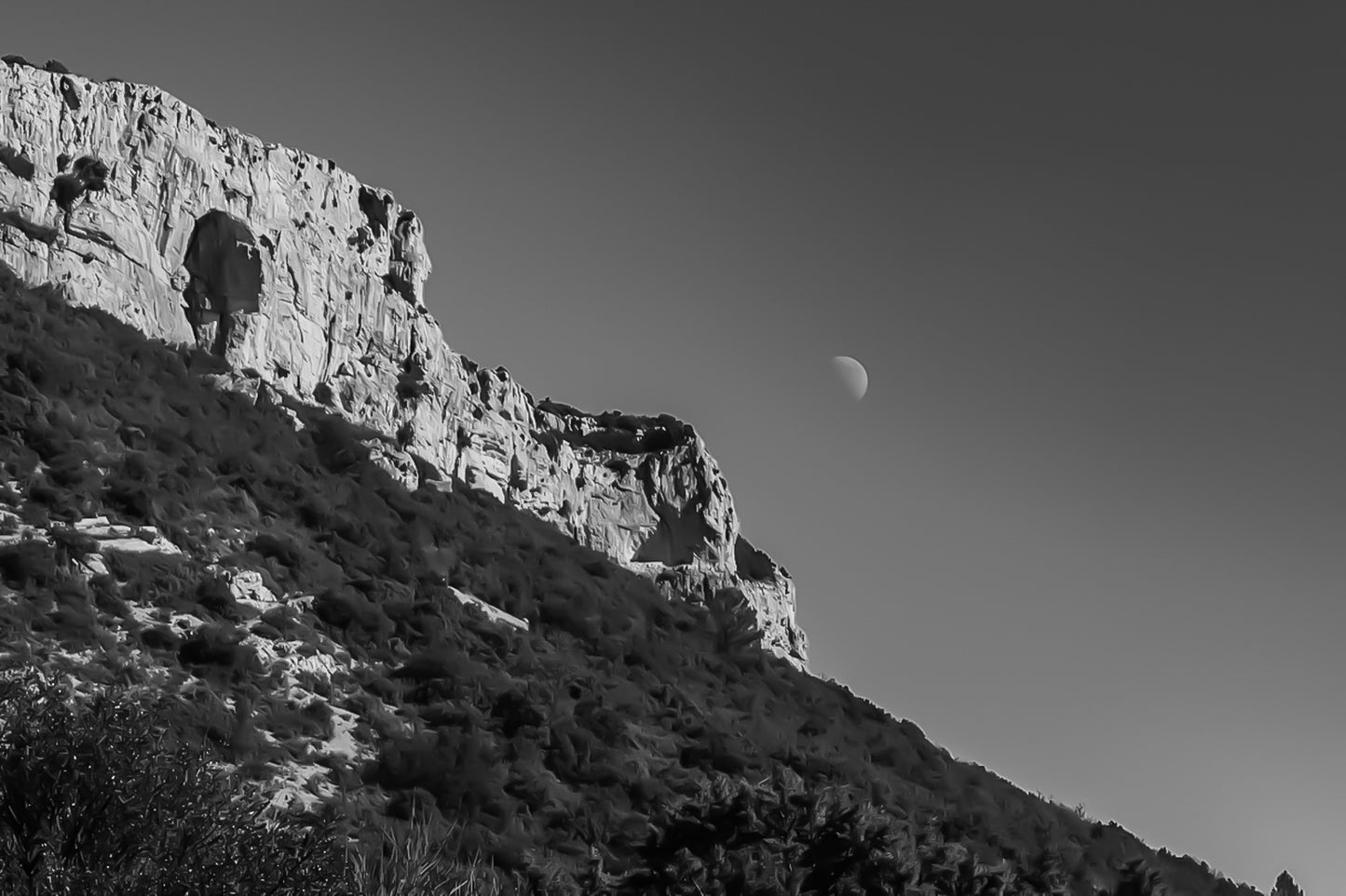 Paroi rocheuse de la Sainte-Baume et lune dans un ciel noir et blanc contrasté, ambiance graphique.
