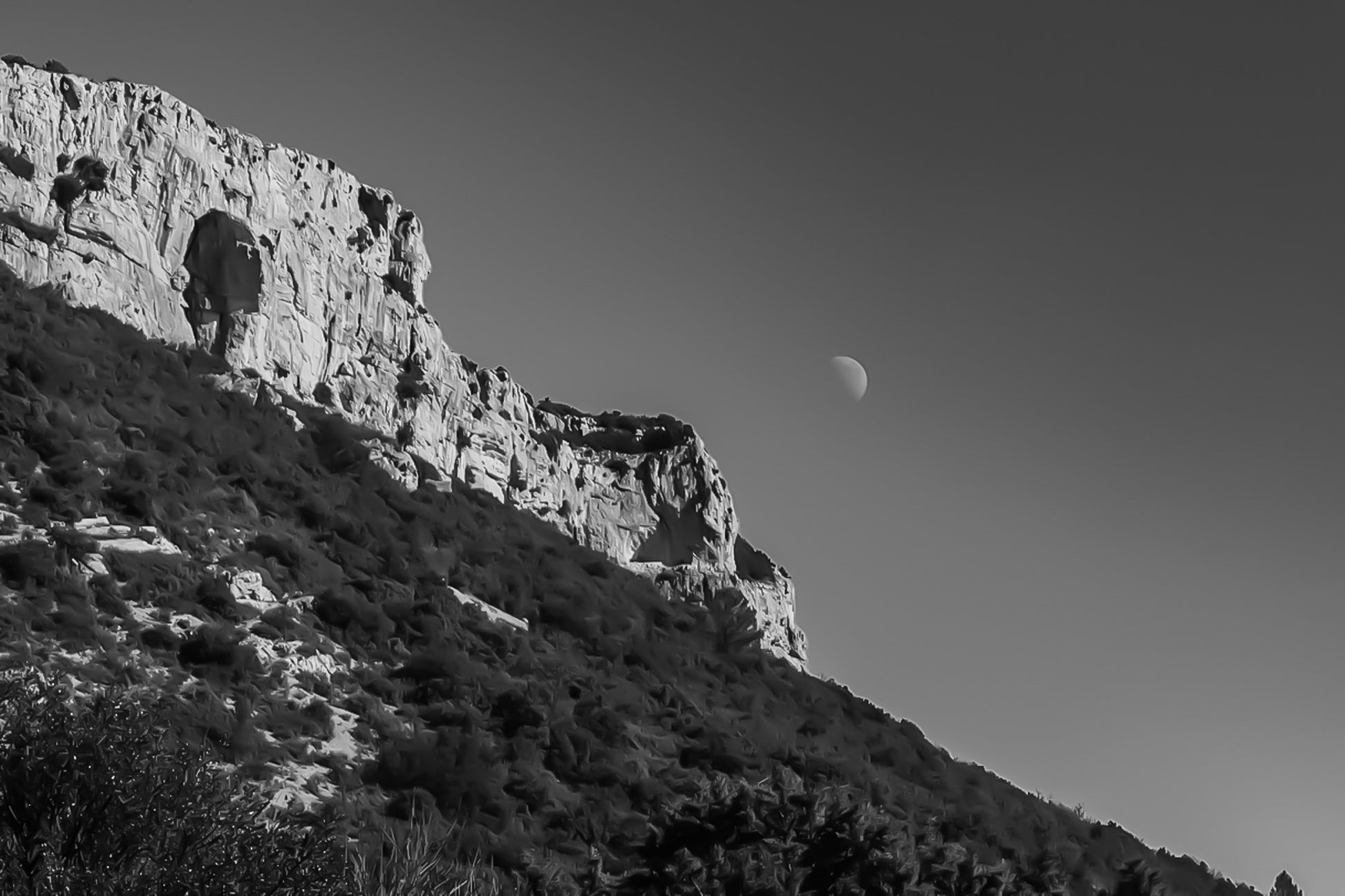 Paroi rocheuse de la Sainte-Baume et lune dans un ciel noir et blanc contrasté, ambiance graphique.