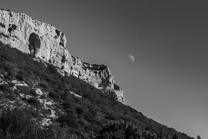 Paroi rocheuse de la Sainte-Baume et lune dans un ciel noir et blanc contrasté, ambiance graphique.
