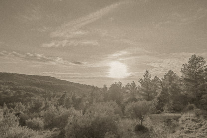 Chemin de garrigue au crépuscule, soleil bas dans un ciel orangé éclairant les buissons et les collines lointaines, vintage