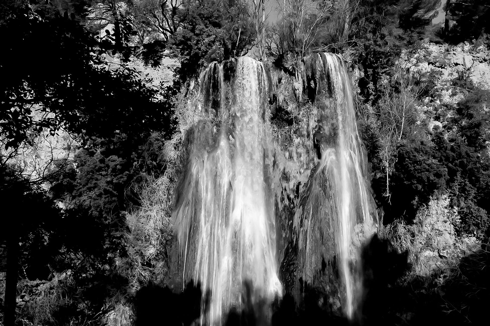 Grande cascade de Sillans tombant en rideaux blancs sur une paroi ocre et moussue, encadrée par la végétation, noir et blanc