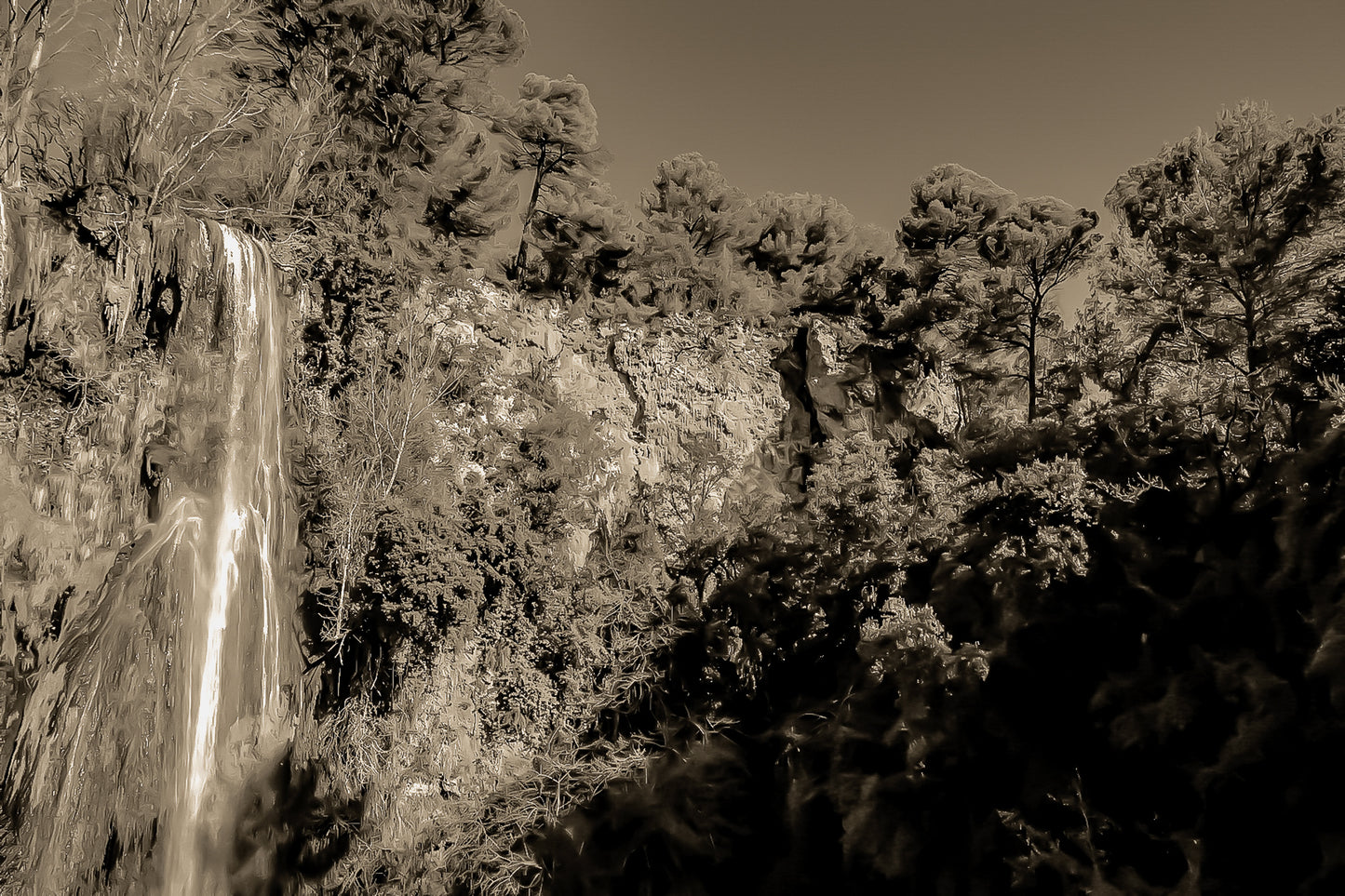 Paroi rocheuse orangée et pins verts dominant la cascade de Sillans sous un ciel bleu intense, version sepia