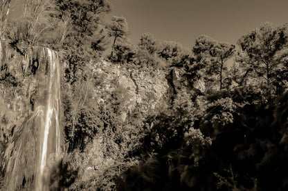 Paroi rocheuse orangée et pins verts dominant la cascade de Sillans sous un ciel bleu intense, vintage