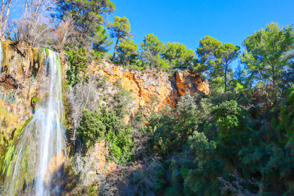 Paroi rocheuse orangée et pins verts dominant la cascade de Sillans sous un ciel bleu intense