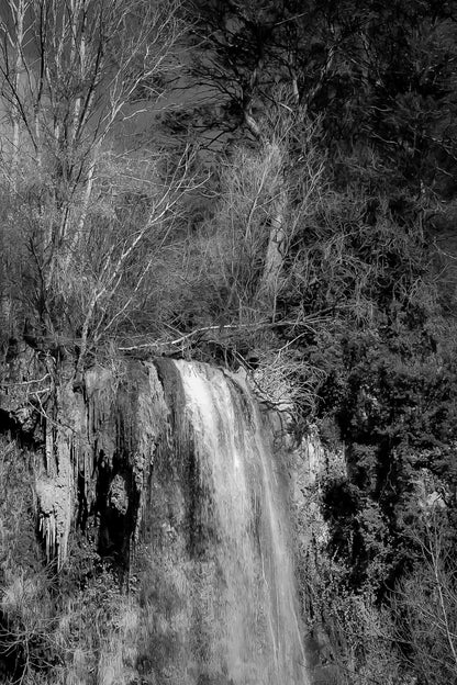 Gros plan vertical sur la cascade de Sillans avec eau ruisselante et mousses vertes accrochées à la falaise, noir et blanc