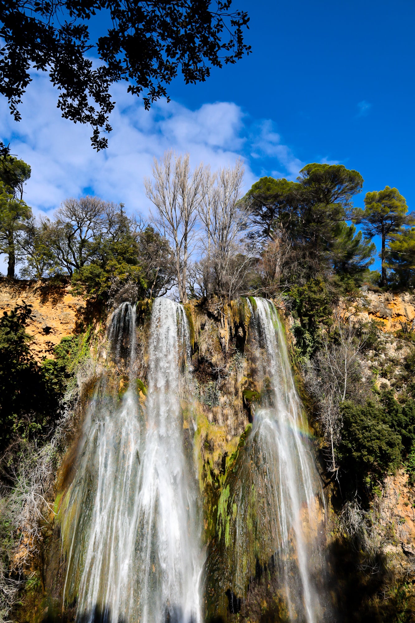 Haute cascade de Sillans se détachant sur un ciel bleu, encadrée par les arbres de la forêt