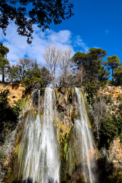 Haute cascade de Sillans se détachant sur un ciel bleu, encadrée par les arbres de la forêt