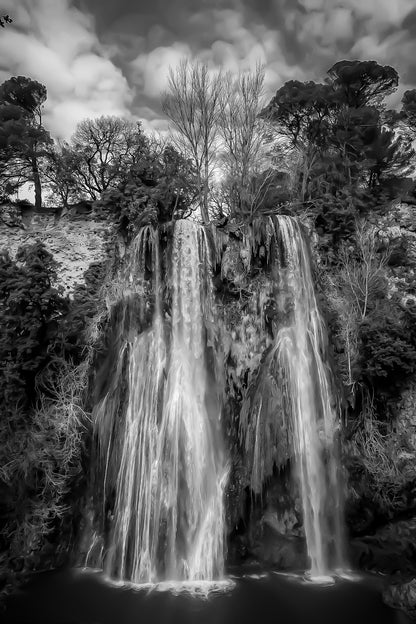 Grande cascade de Sillans se jetant dans un bassin vert émeraude entouré de falaises et de végétation, noir et blanc