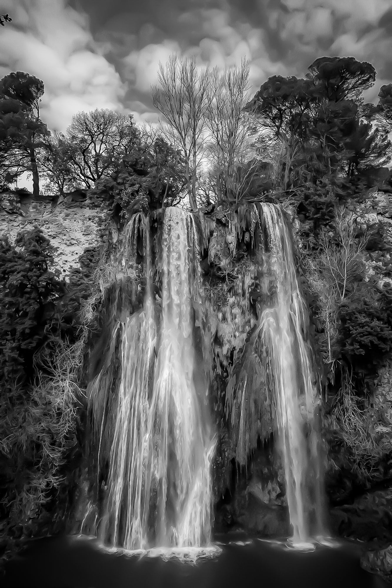 Grande cascade de Sillans se jetant dans un bassin vert émeraude entouré de falaises et de végétation, noir et blanc