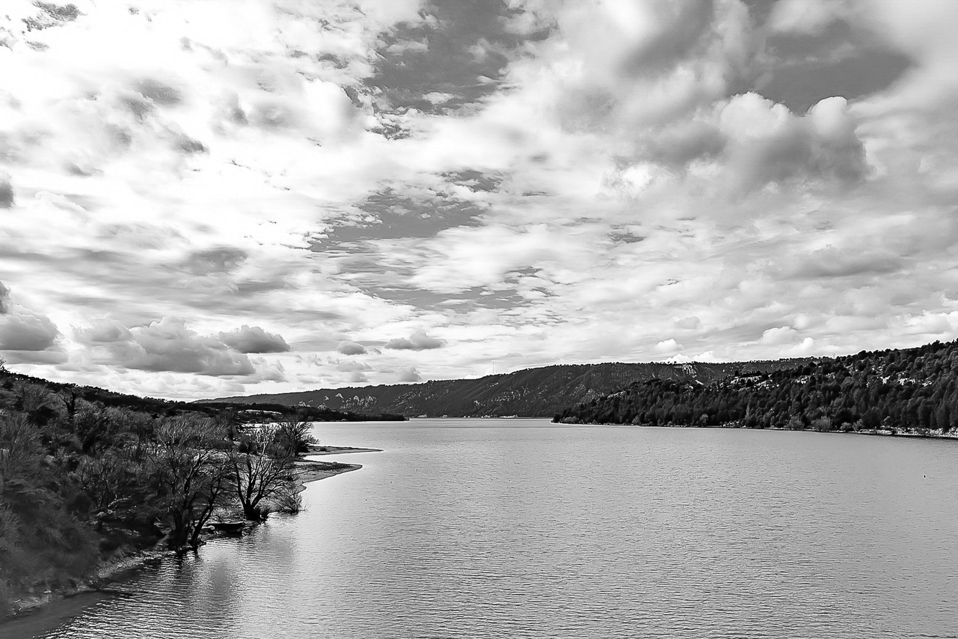Large vue sur le lac de Sainte-Croix depuis un pont, rives boisées et grand ciel nuageux, noir et blanc