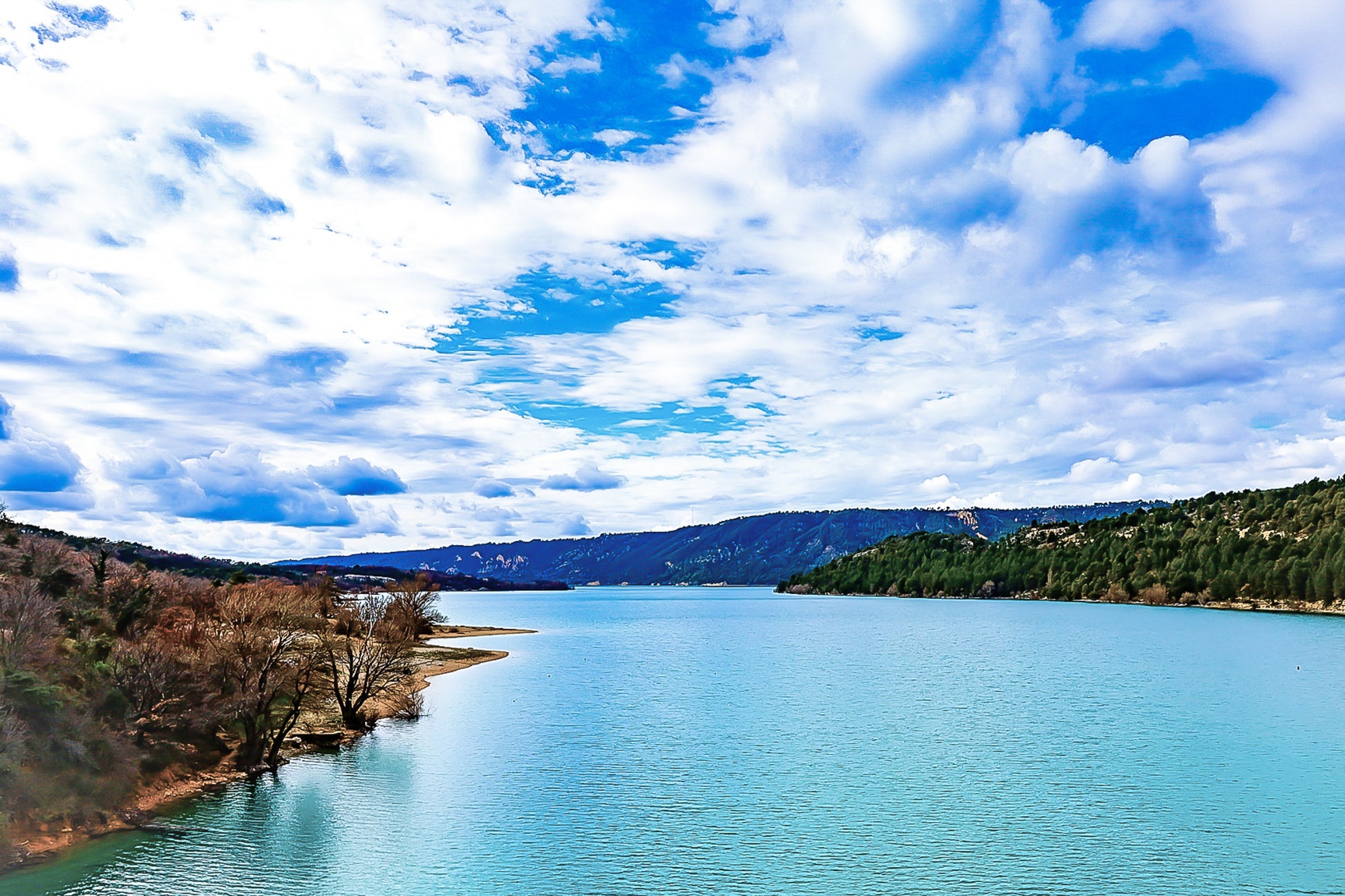 Large vue sur le lac de Sainte-Croix depuis un pont, rives boisées et grand ciel nuageux