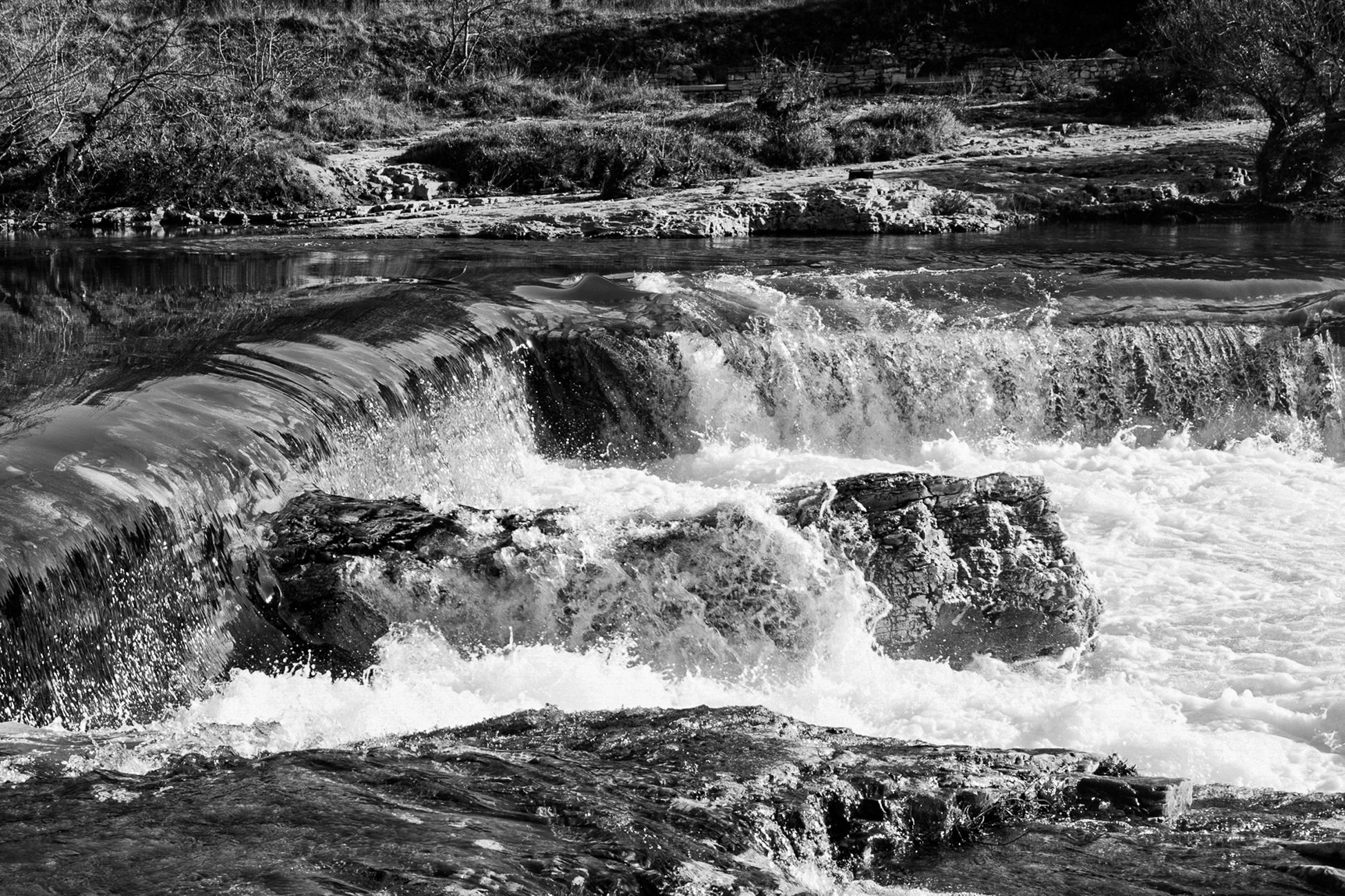 Chute de la cascade du Sautadet vue de près, rideau d’eau doré glissant sur la roche avant de se briser en écume blanche, noir et blanc