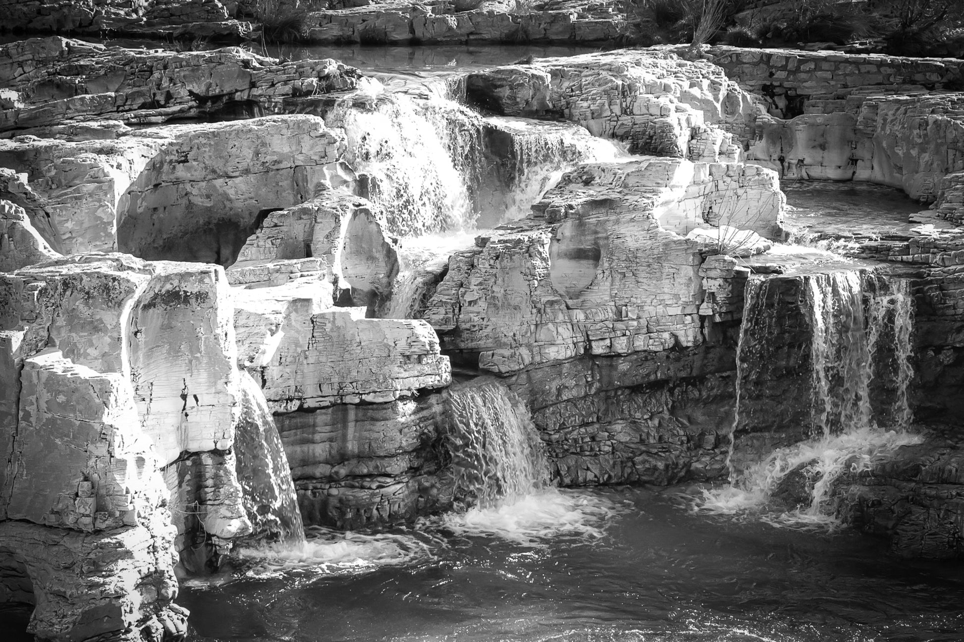 Ensemble de chutes superposées tombant dans un bassin turquoise à la cascade du Sautadet, noir et blanc