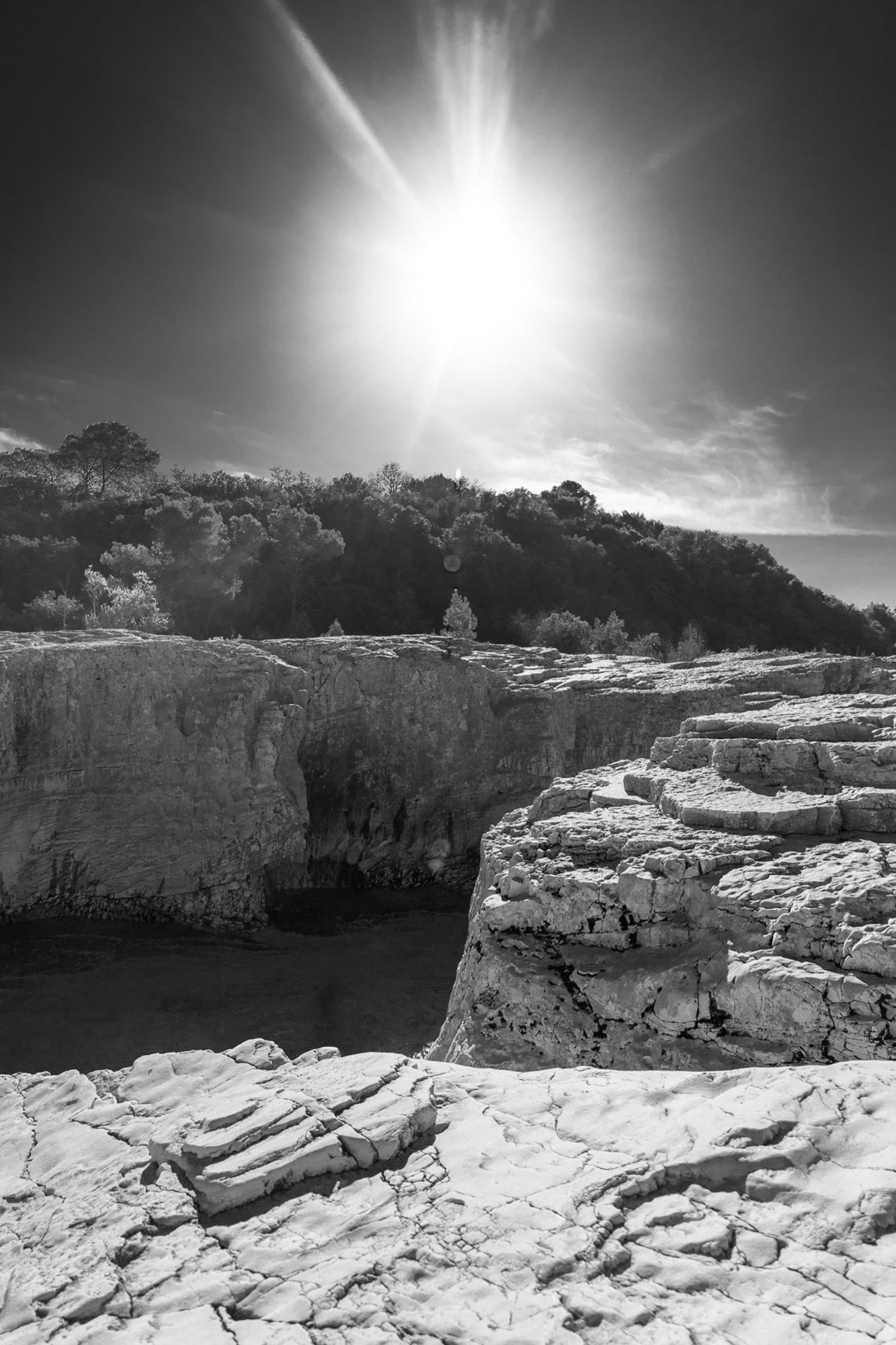 Soleil au zénith au-dessus des falaises claires et de l’eau bleu profond à la cascade du Sautadet, noir et blanc
