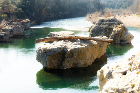 Gros rocher au milieu de la rivière Cèze avec un tronc posé en travers à la cascade du Sautadet