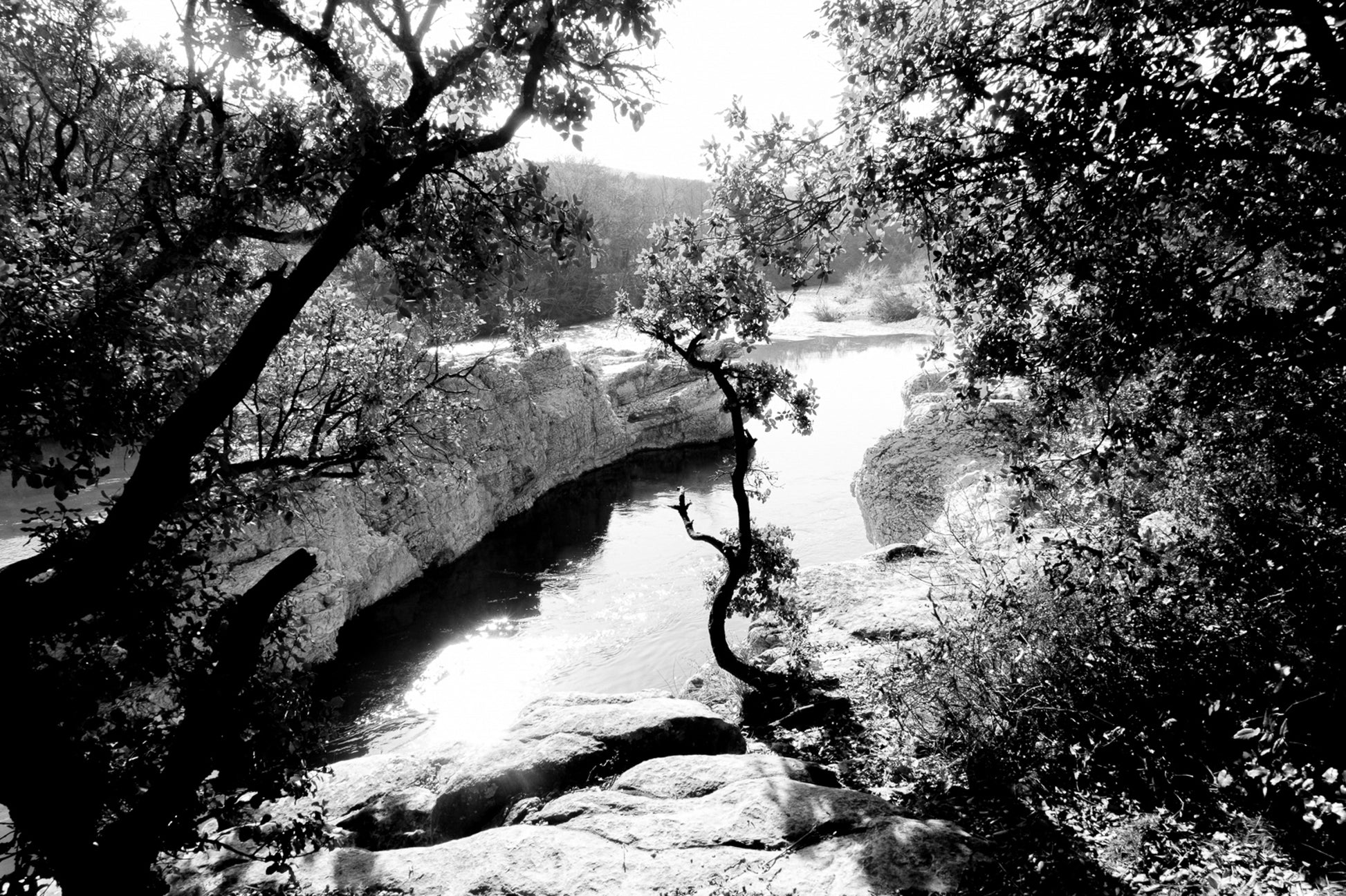 Courbe de la rivière Cèze vue à travers un encadrement d’arbres et de rochers à la cascade du Sautadet, noir et blanc