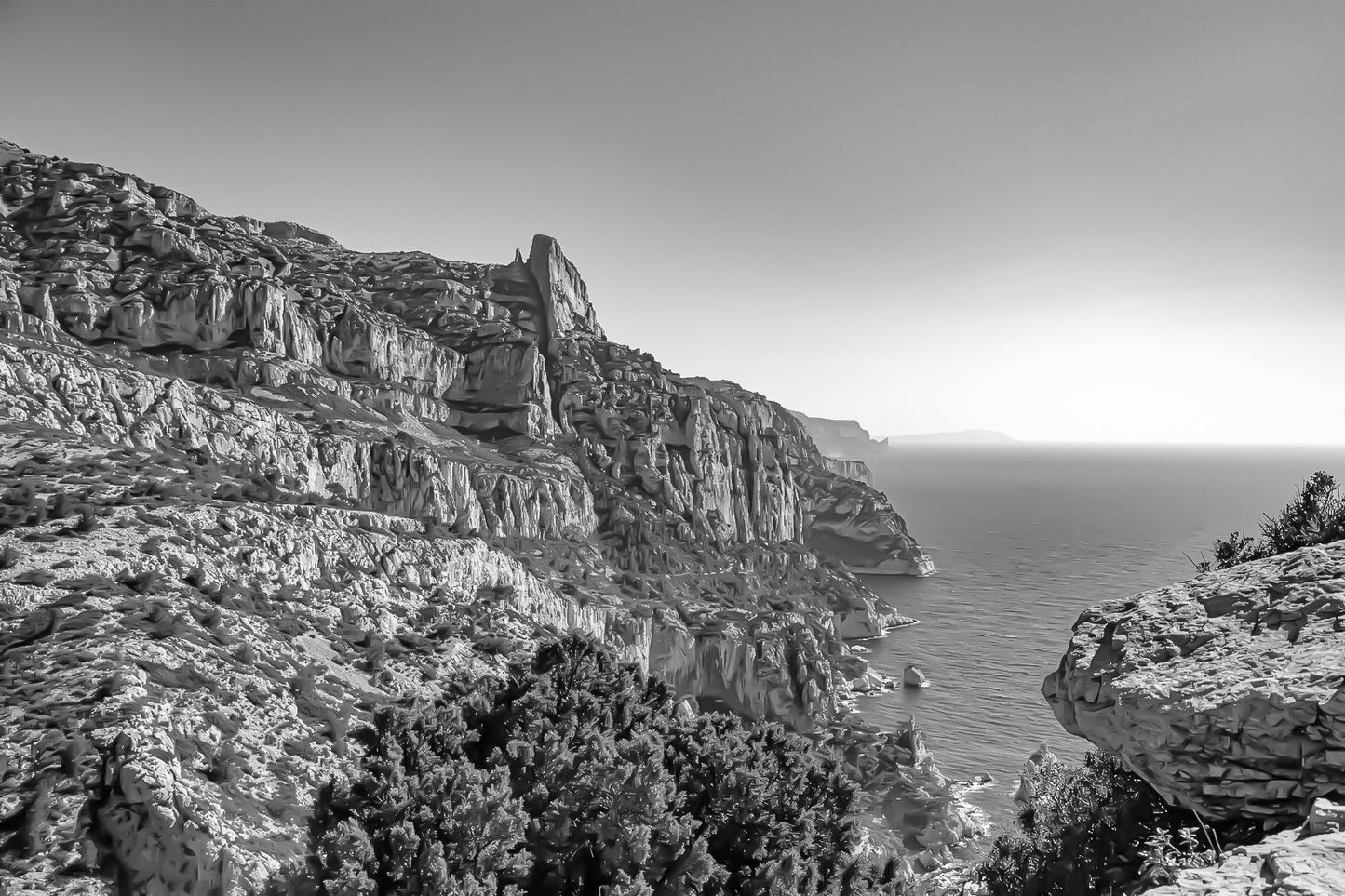 Falaises monumentales des calanques de Sugiton plongeant vers la Méditerranée par ciel bleu profond, noir et blanc