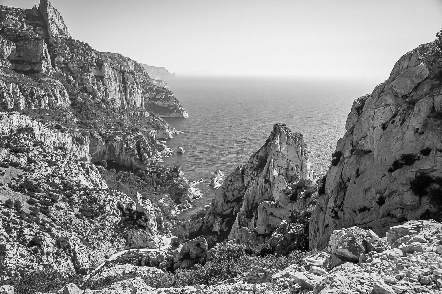 Vue plongeante entre deux parois rocheuses sur l’eau turquoise de la calanque de Sugiton, noir et blanc