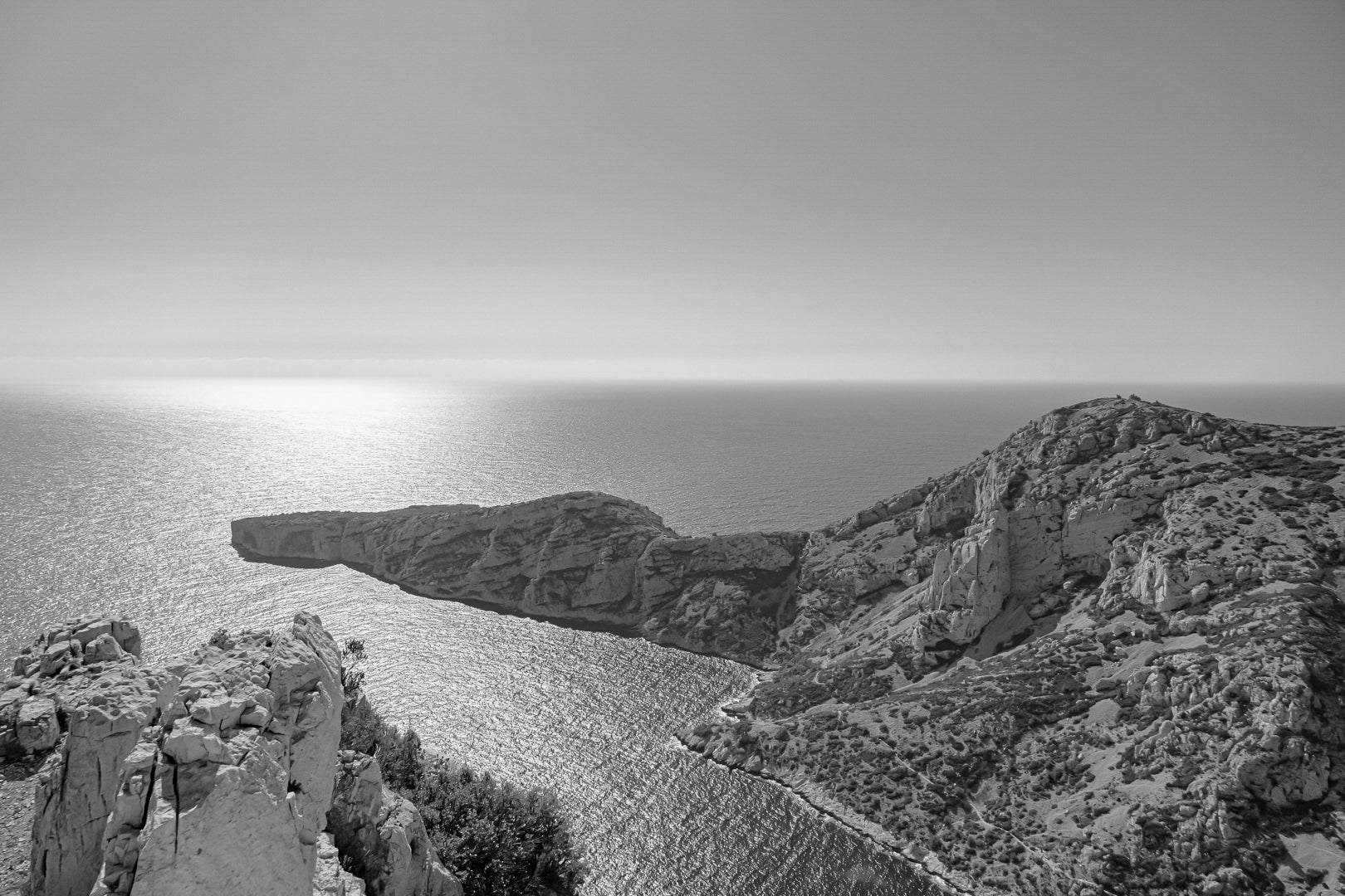 Éperon rocheux avançant dans la mer scintillante au large des calanques de Marseille, noir et blanc