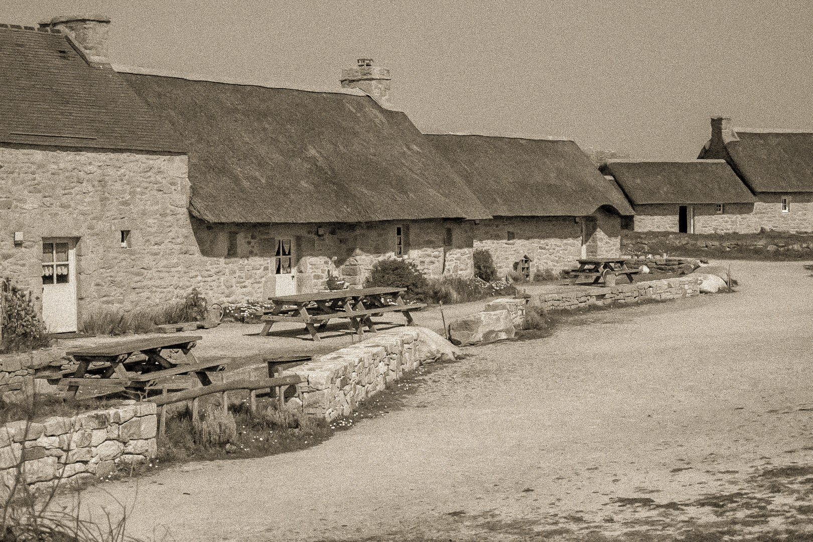 Longère de Meneham avec tables en bois, mur de pierre et toit de chaume, traitement vintage sépia - Kerlouan, Finistère