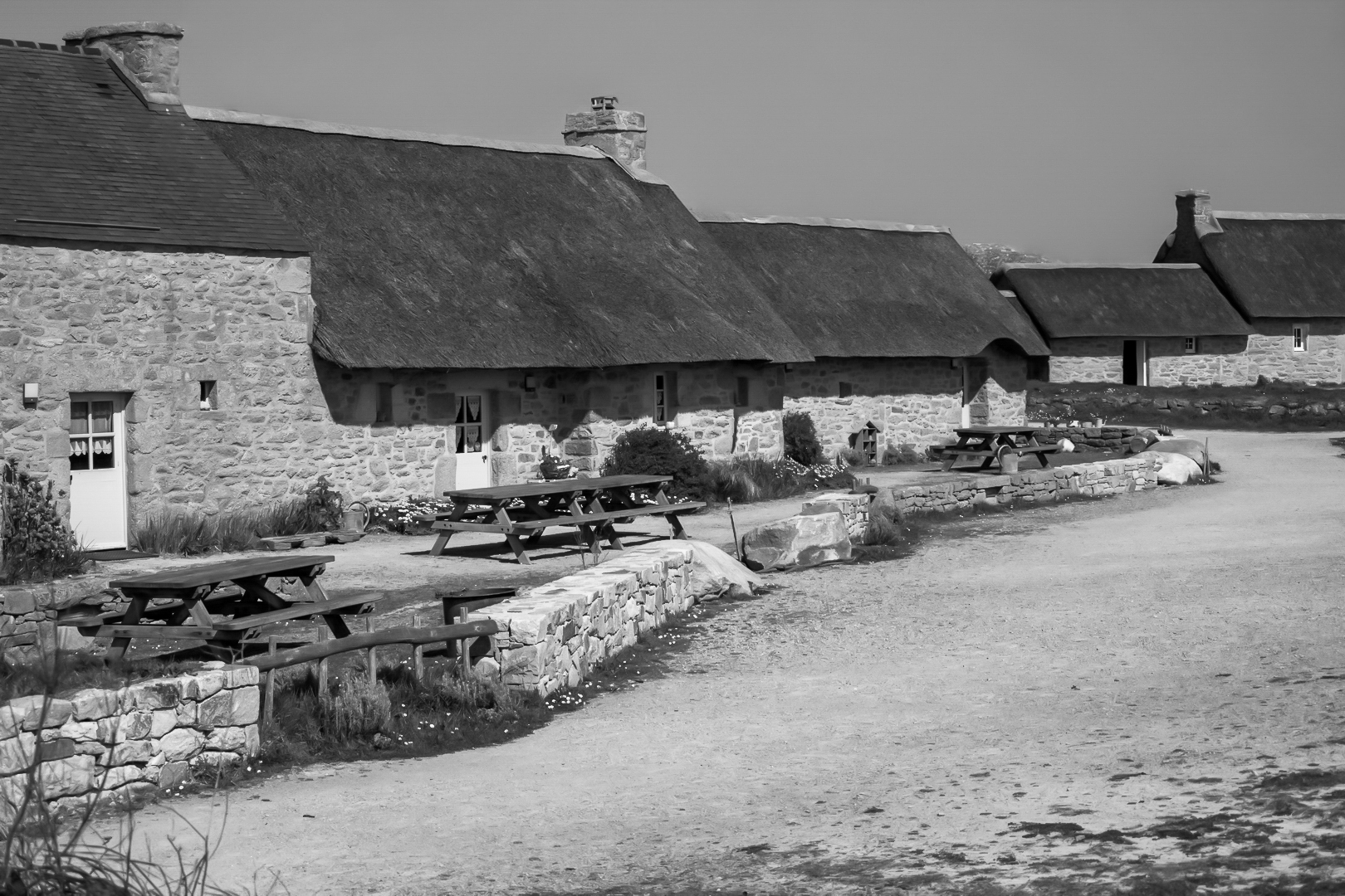 Longère de Meneham avec tables en bois, mur de pierre et toit de chaume, noir et blanc - Kerlouan, Finistère