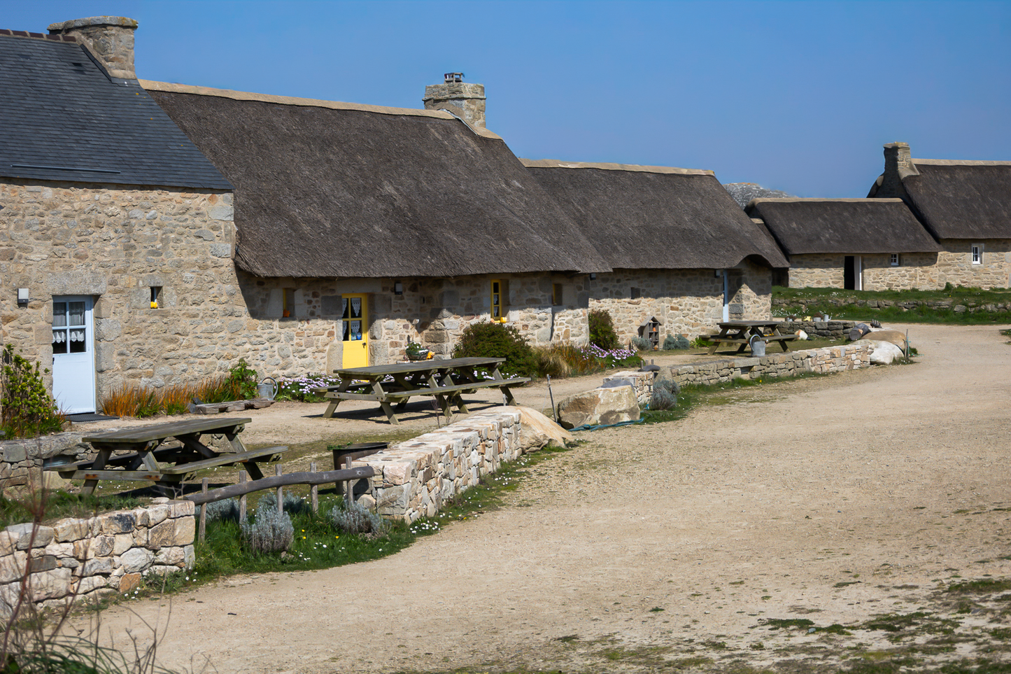 Longère de Meneham avec tables en bois, mur de pierre et toit de chaume, couleur - Kerlouan, Finistère