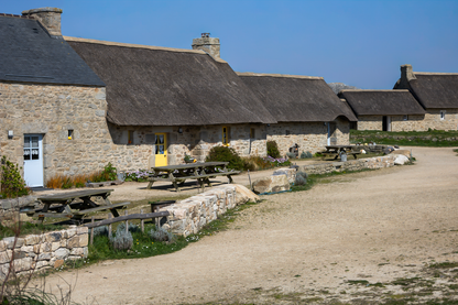 Longère de Meneham avec tables en bois, mur de pierre et toit de chaume, couleur - Kerlouan, Finistère