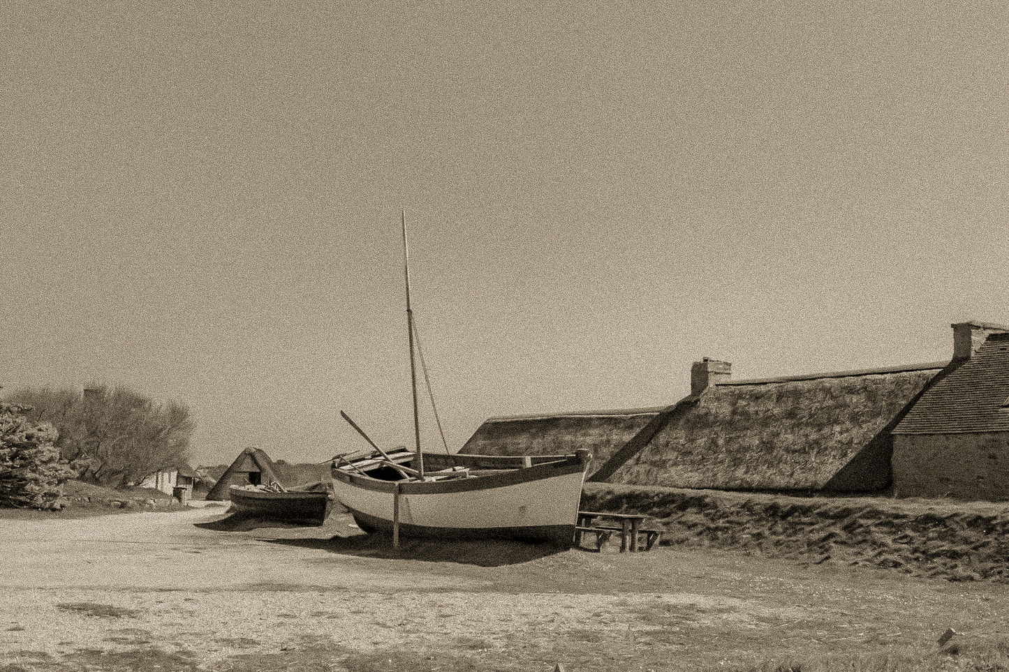 Barques tirées au sec devant les toits de chaume et murets de pierre à Meneham, ambiance ancienne en sépia.