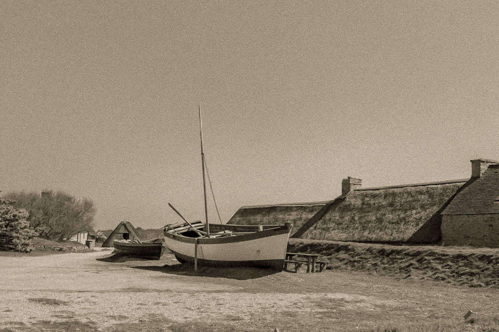 Barques tirées au sec devant les toits de chaume et murets de pierre à Meneham, ambiance ancienne en sépia