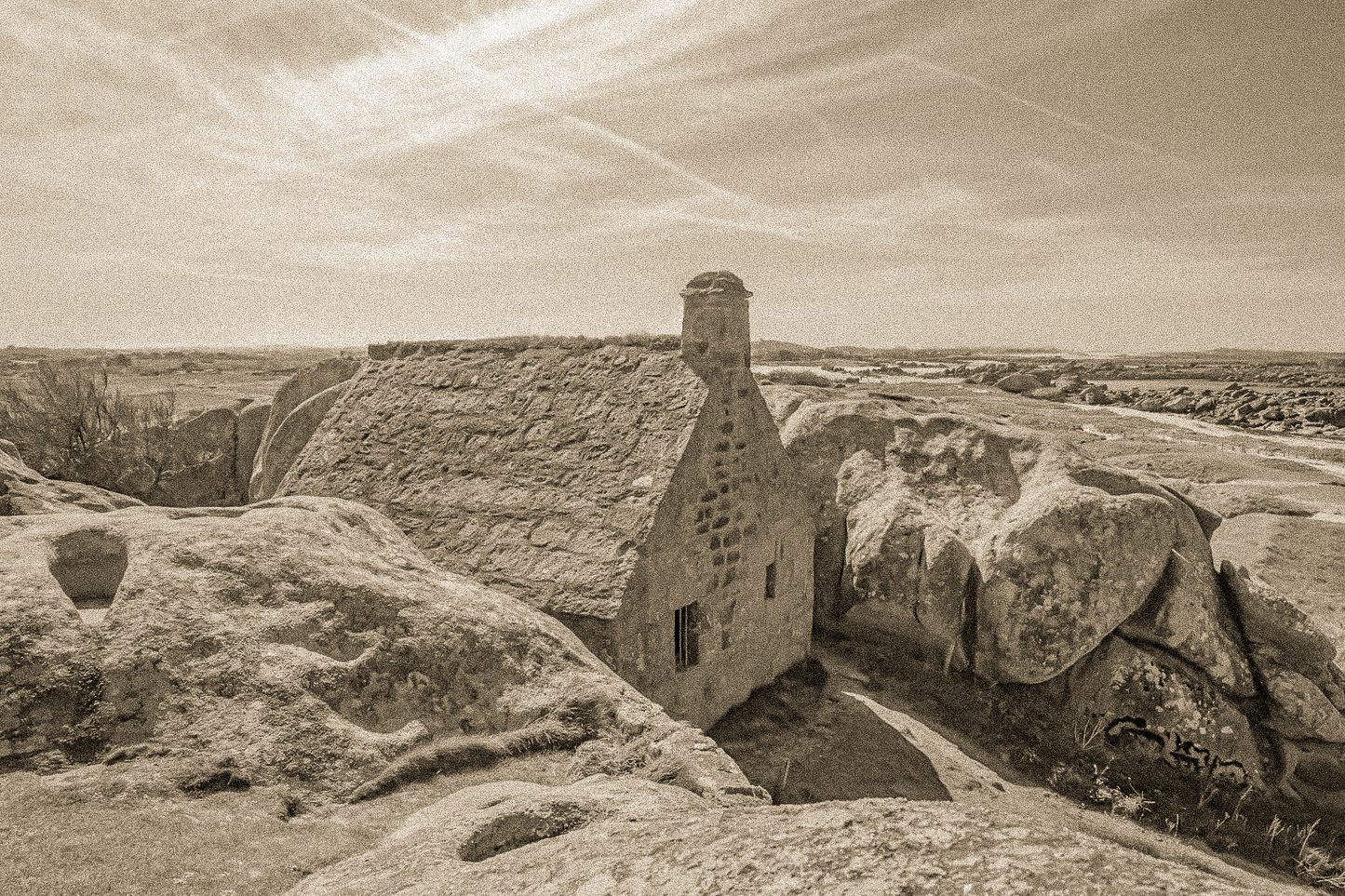 La maison emblématique de Meneham nichée entre deux énormes blocs de granit, vue d’ensemble en sépia vintage.