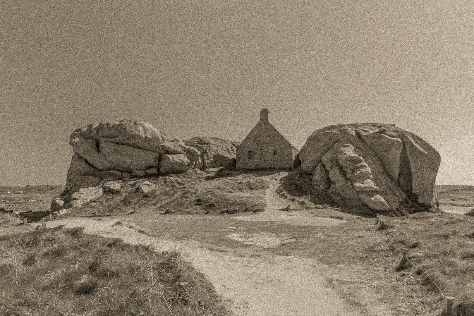 Façade de la maison des gardes encadrée par deux rochers monumentaux, Meneham (Kerlouan), traitement sepia