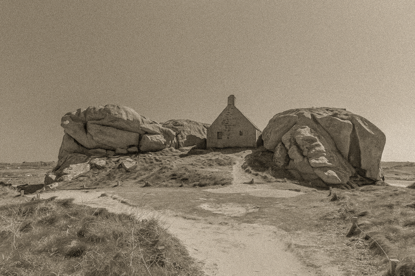 Façade de la maison des gardes encadrée par deux rochers monumentaux, traitement sépia, Meneham (Kerlouan)