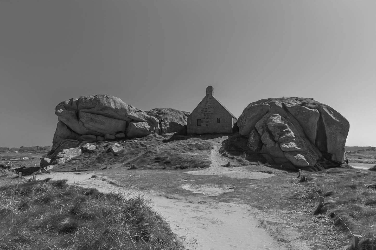Façade de la maison des gardes encadrée par deux rochers monumentaux, noir et blanc, Meneham (Kerlouan)