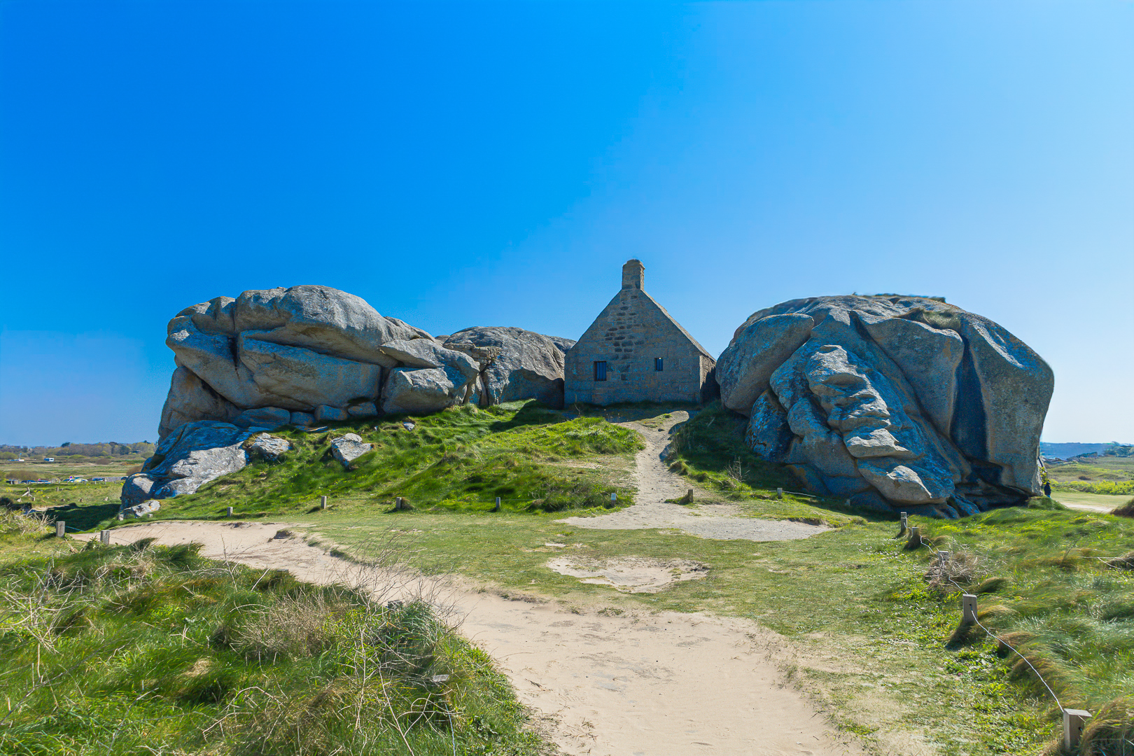 Façade de la maison des gardes encadrée par deux rochers monumentaux, Meneham (Kerlouan), couleur