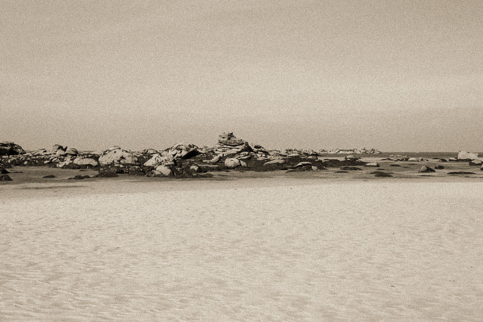 Grande plage claire avec rochers épars et ligne d’horizon marine, ambiance sépia vintage à Meneham