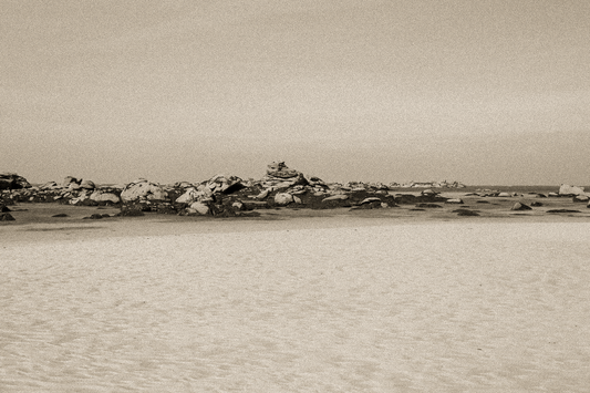 Grande plage claire avec rochers épars et ligne d’horizon marine, ambiance sépia vintage à Meneham