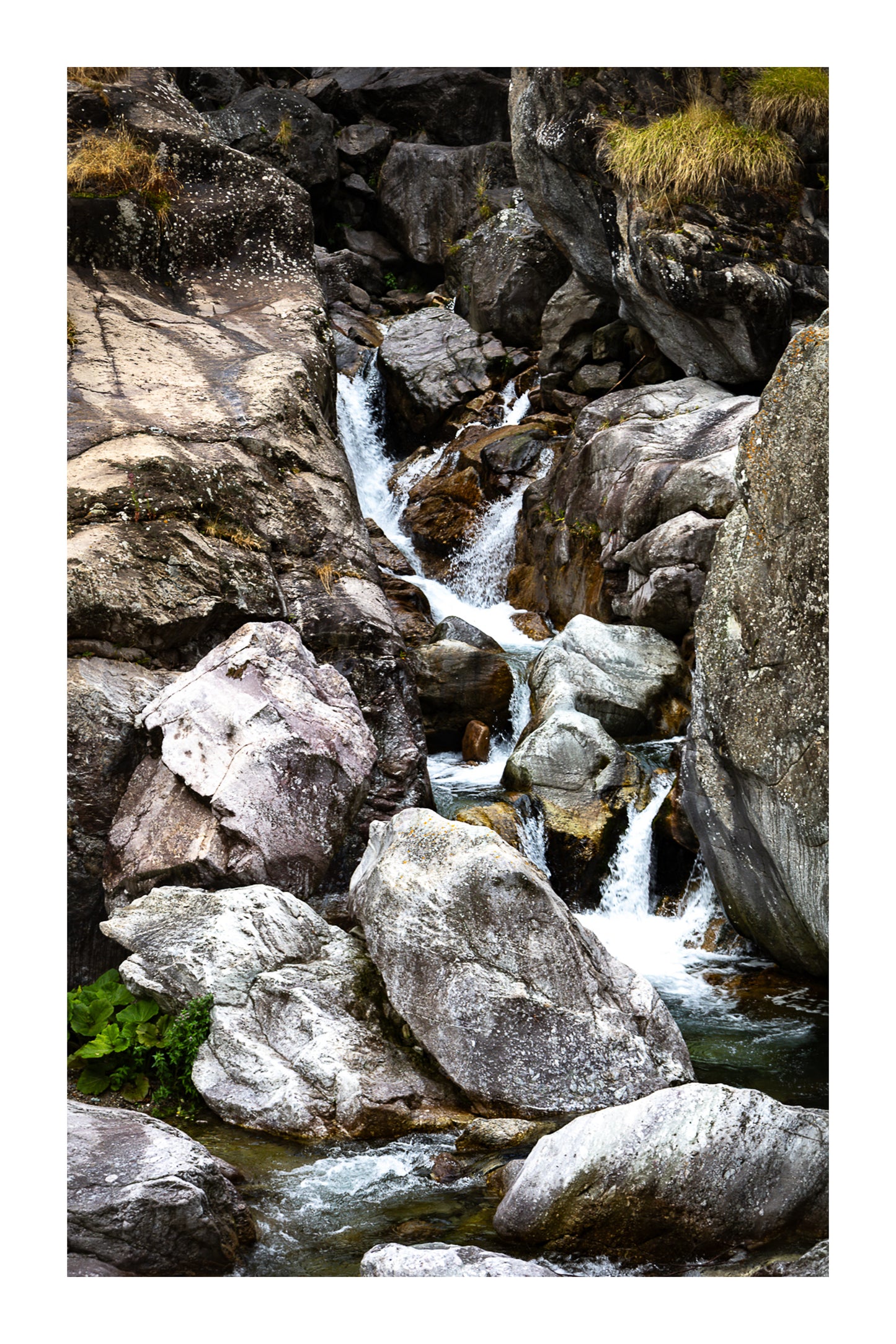 Cascade du Ray entre de gros blocs rocheux, eau qui s’écoule en marches successives, couleur avec bordure