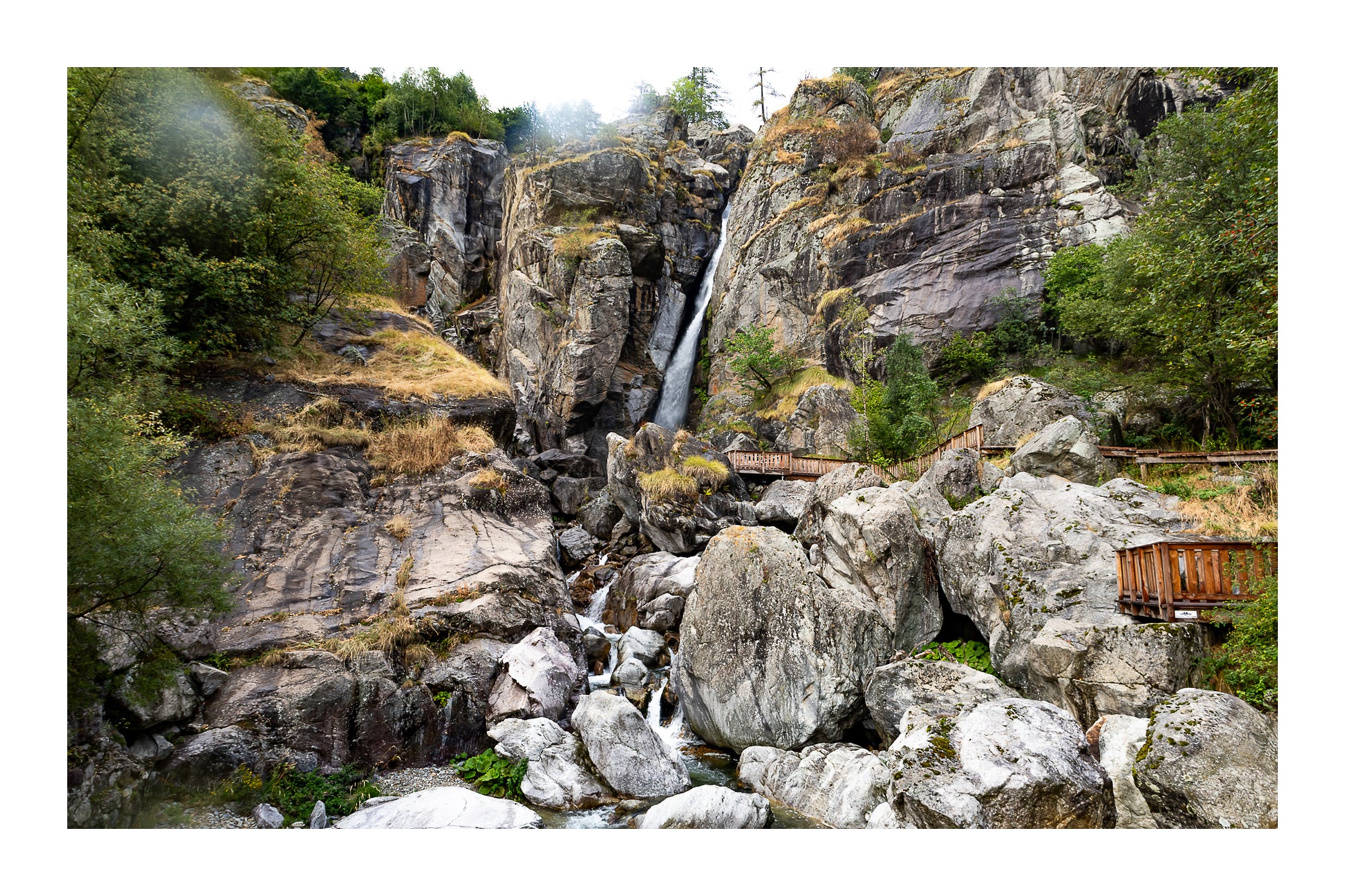 Panorama de la cascade du Ray entourée de falaises et de blocs rocheux, ambiance montagneuse, couleur avec bordure