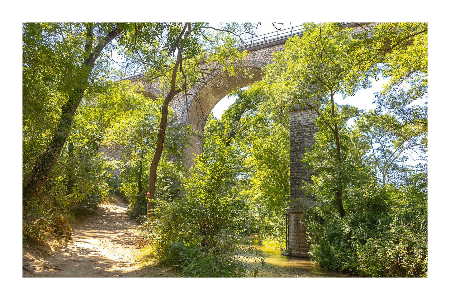Viaduc de pierre traversant une vallée boisée au-dessus de la rivière de l’Arc avec bordure