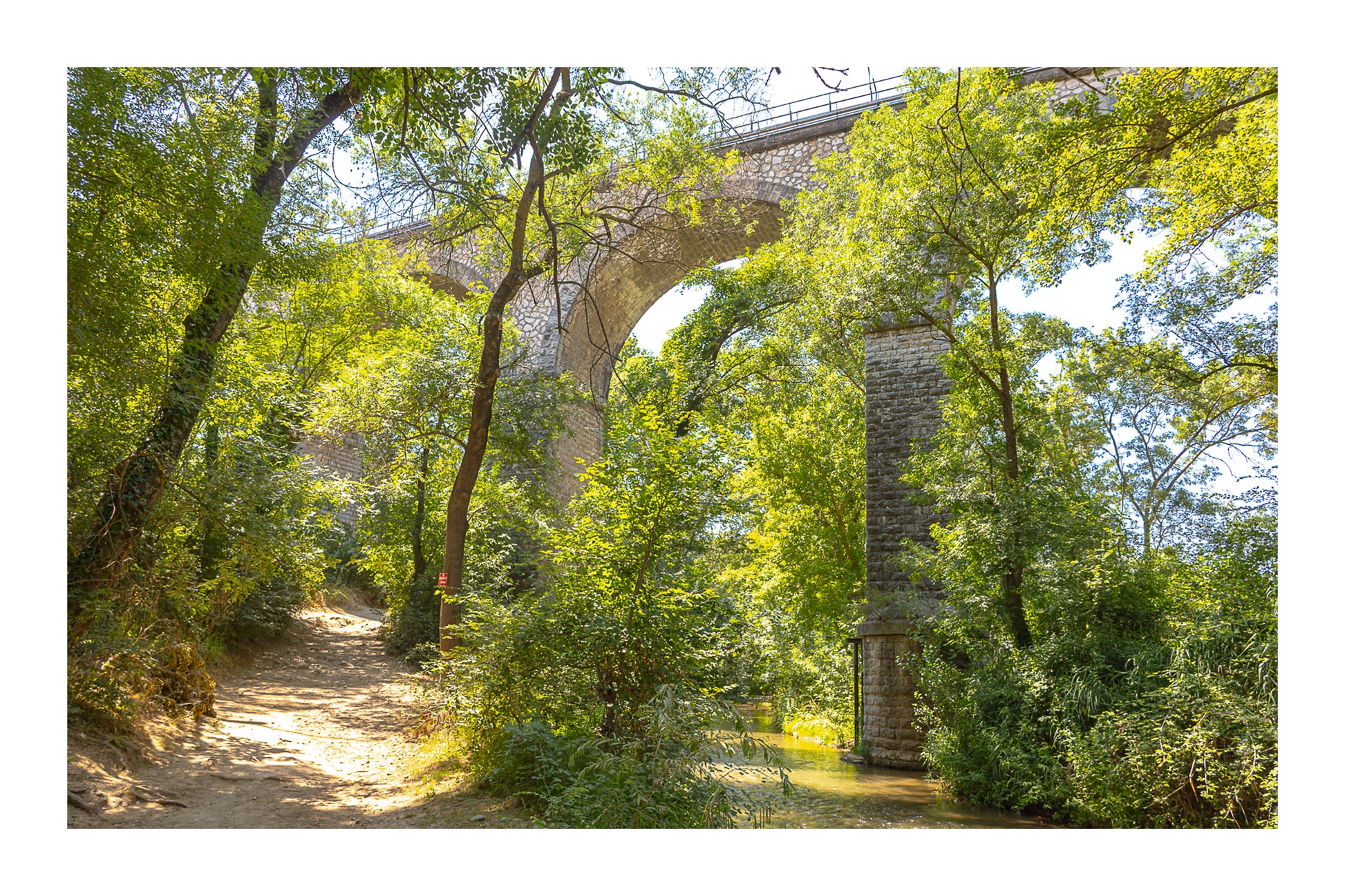Viaduc de pierre traversant une vallée boisée au-dessus de la rivière de l’Arc avec bordure