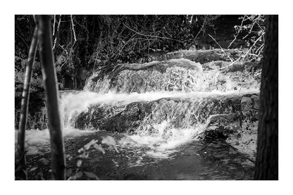 Petite cascade aux eaux émeraude sur la rivière de l’Arc entourée de végétation à Aix-en-Provence, noir et blanc avec bordure