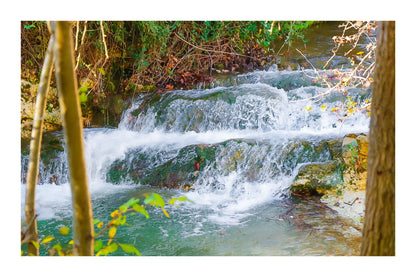 Petite cascade aux eaux émeraude sur la rivière de l’Arc entourée de végétation à Aix-en-Provence avec bordure