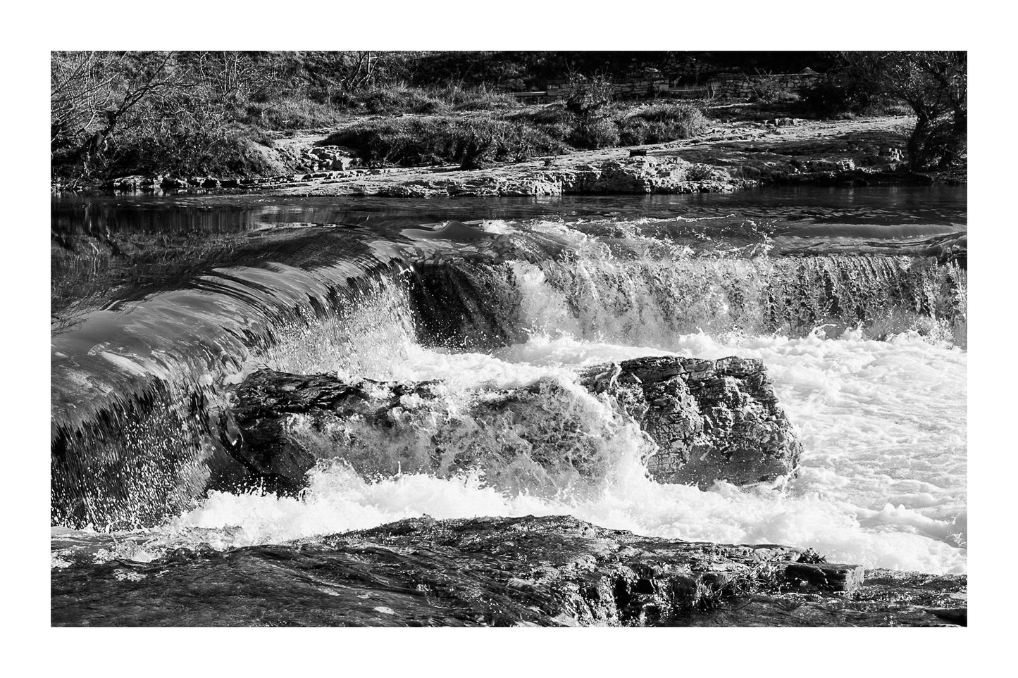 Chute de la cascade du Sautadet vue de près, rideau d’eau doré glissant sur la roche avant de se briser en écume blanche, noir et blanc avec bordure