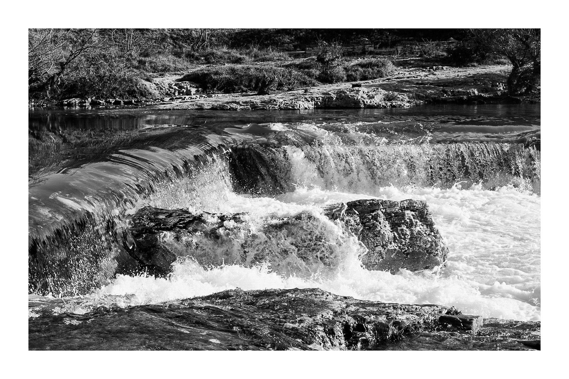 Chute de la cascade du Sautadet vue de près, rideau d’eau doré glissant sur la roche avant de se briser en écume blanche, noir et blanc avec bordure