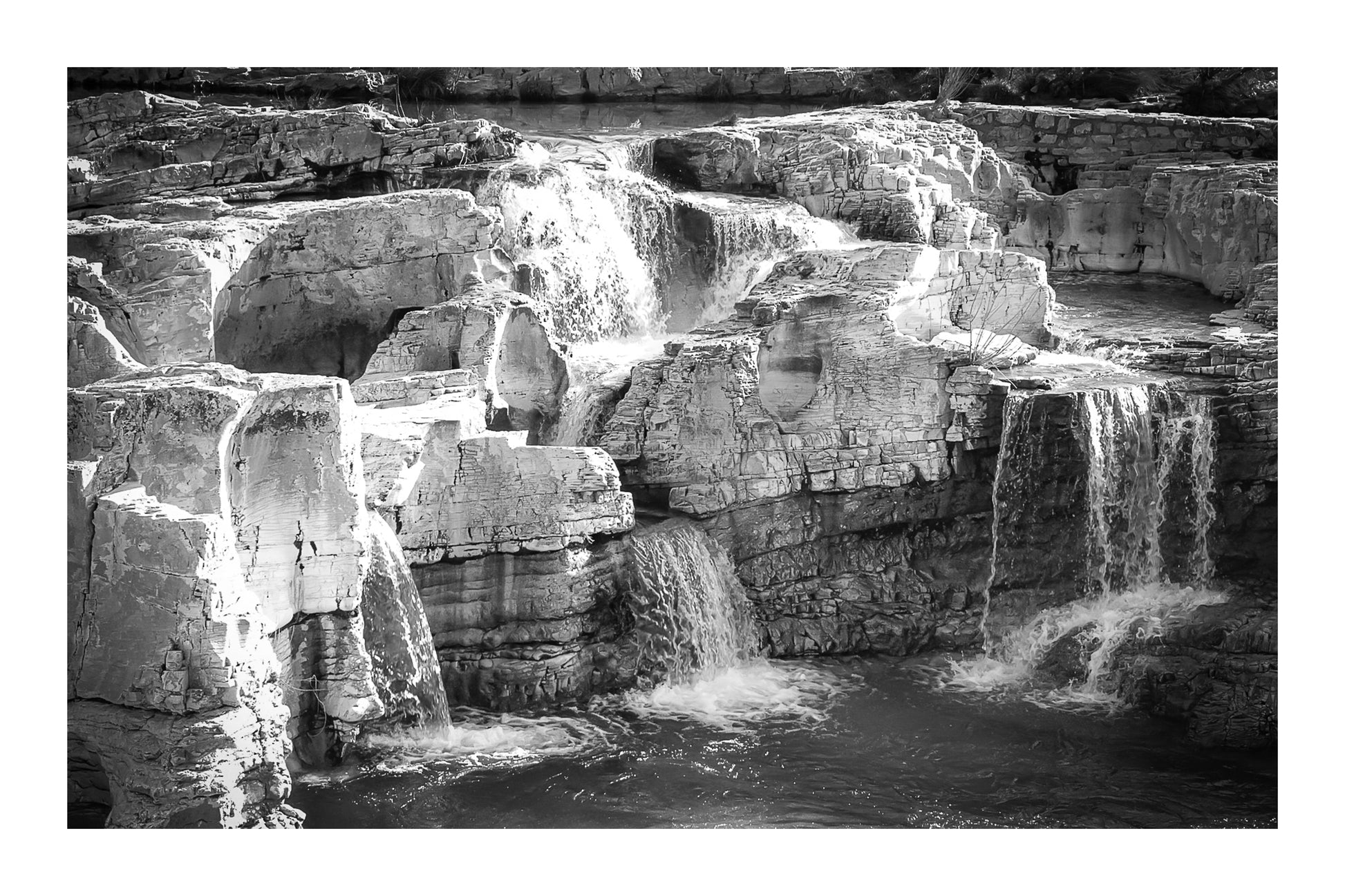 Ensemble de chutes superposées tombant dans un bassin turquoise à la cascade du Sautadet, noir et blanc avec bordure
