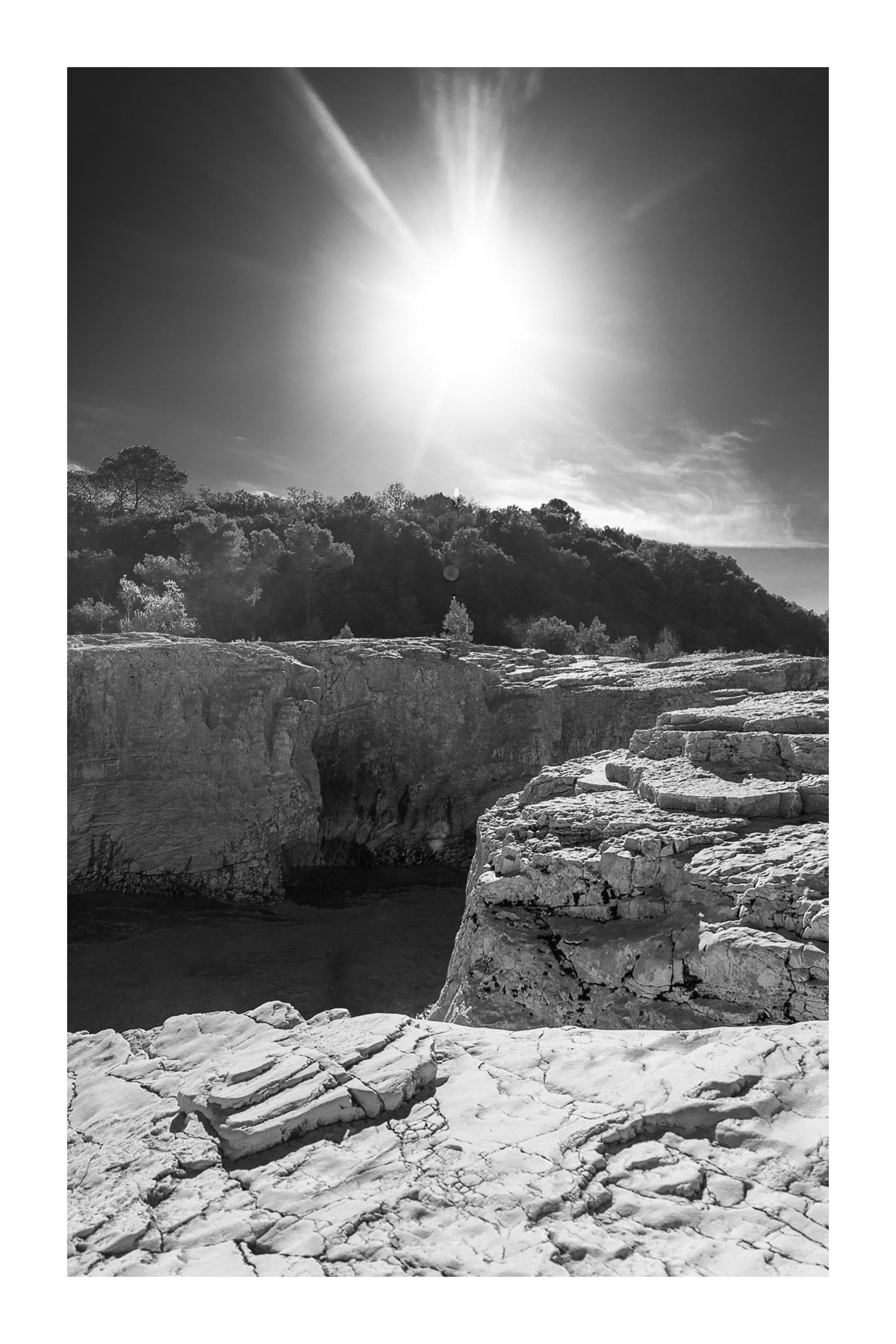 Soleil au zénith au-dessus des falaises claires et de l’eau bleu profond à la cascade du Sautadet, noir et blanc avec bordure