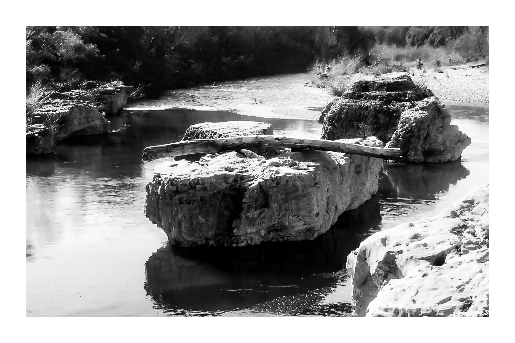Gros rocher au milieu de la rivière Cèze avec un tronc posé en travers à la cascade du Sautadet, noir et blanc avec bordure