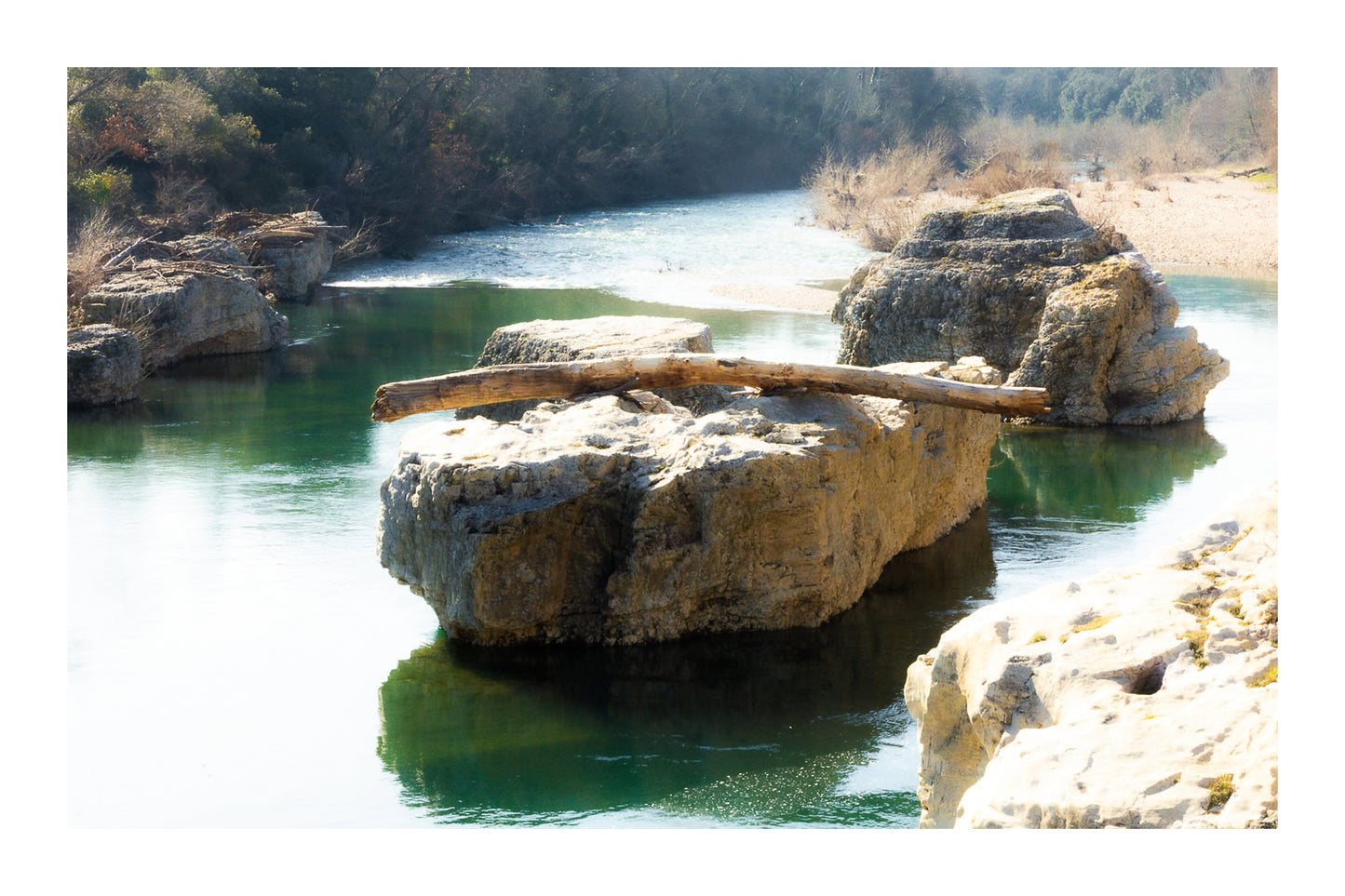 Gros rocher au milieu de la rivière Cèze avec un tronc posé en travers à la cascade du Sautadet avec bordure